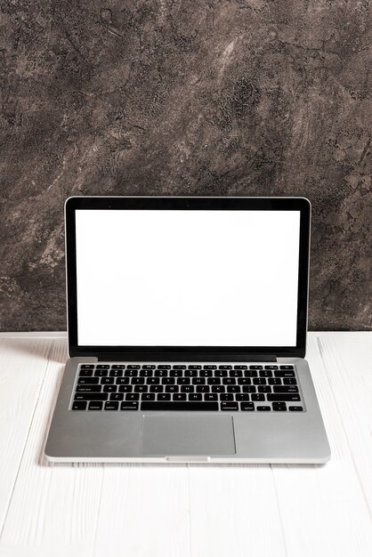 Laptop with blank white screen on white wooden table against concrete