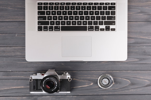 Free photo laptop with camera and compass on wooden table