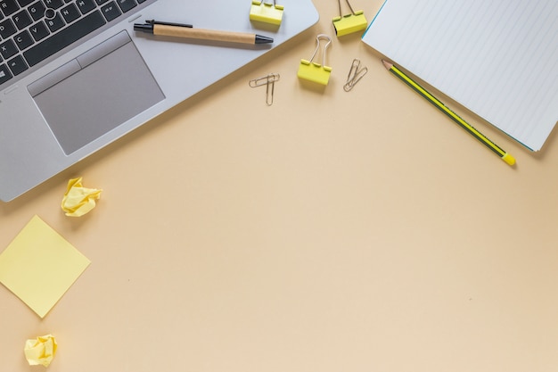 Бесплатное фото Ноутбук с ручкой; карандаш; скрепки; заметки и спиральный блокнот на бежевом фоне