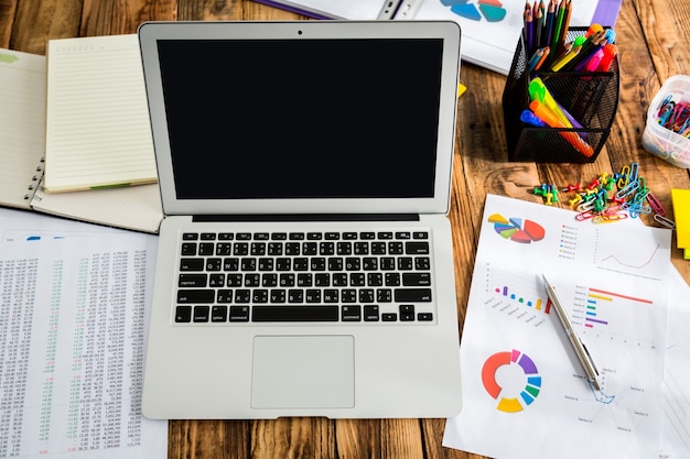 Laptop with pie charts next to it and other papers