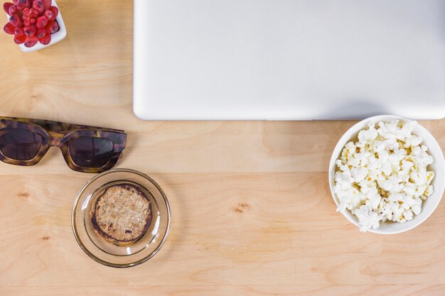 Laptop with popcorn and sunglasses on table 