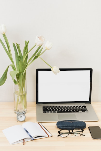 Laptop with tulips in vase on wooden table