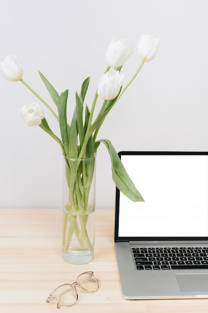 Laptop with white tulips in vase on table