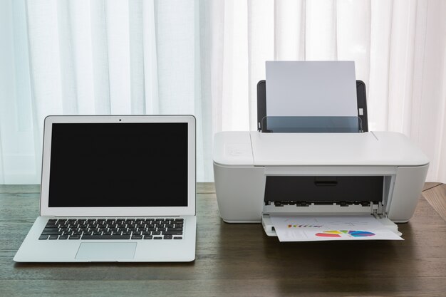 Laptop on a wooden table with a printer