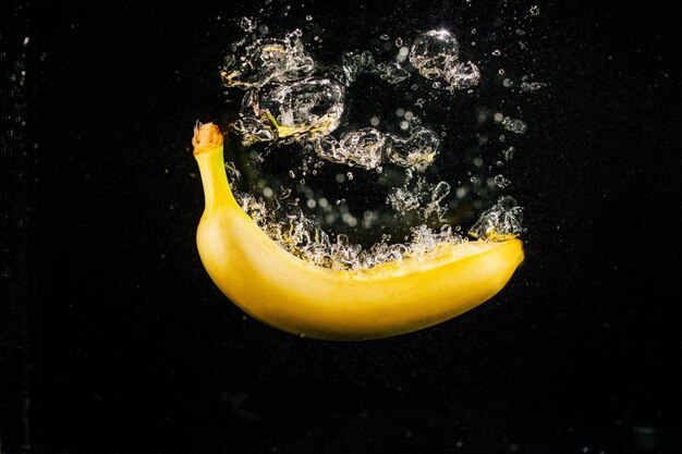 Large bubbles raise from banana while it falls in water on black background