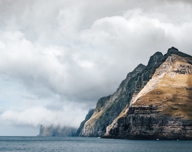 Large cliff surrounded by the water under the clouds