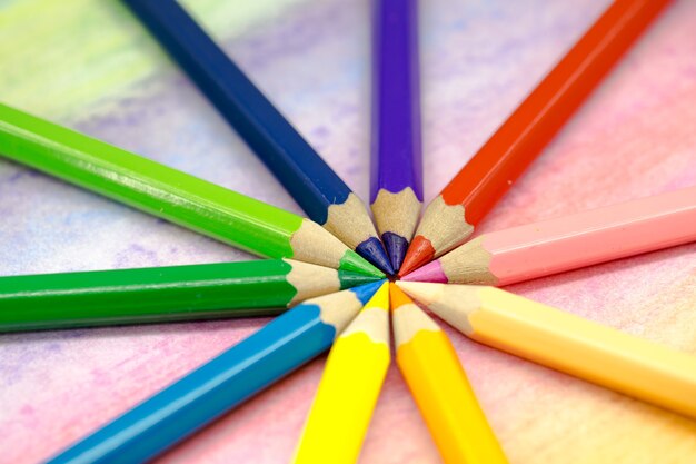 Large colored pencils stacked in a circle close-up on a colored background with colored pencils