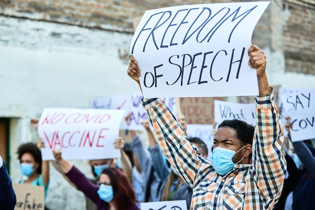 Large group of displeased people protesting during coronavirus pandemic Focus is on black man holding a banner with Freedom of speech inscription