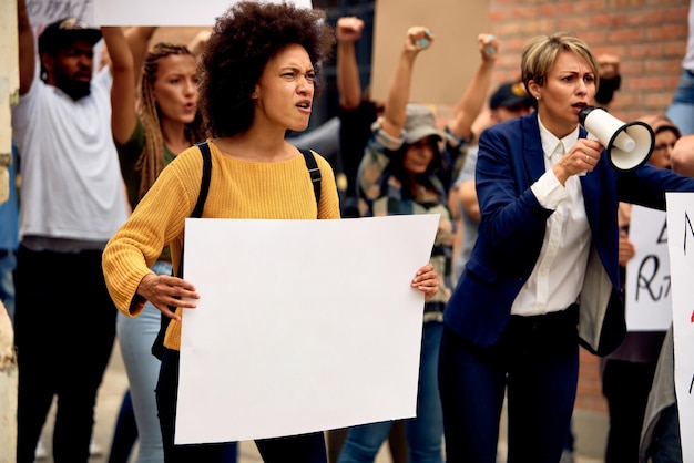 Large group of displeased protesters marching at demonstrations on the streets Focus is on African American woman holding blank placard Copy space