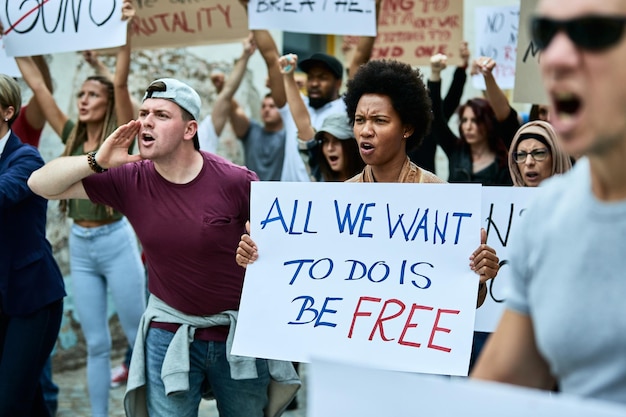 Foto gratuita un folto gruppo di manifestanti scontenti che partecipano a manifestazioni pubbliche contro il razzismo il focus è sulla donna di colore che tiene uno striscione