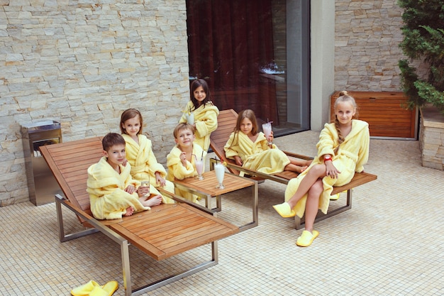 Большая компания друзей, которые пьют молочные коктейли. Счастливые улыбающиеся мальчики и девочки в желтых махровых халатах.