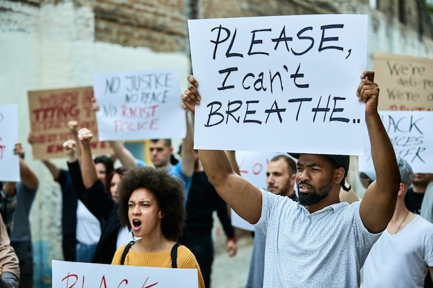 ブラック・ライヴズ・マターの抗議に参加している大勢の人々が、プラカードを持っている黒人男性に焦点を当てています。