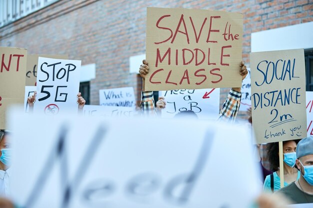 Большая группа людей, протестующих за права человека во время пандемии COVID-19, в центре внимания баннер «Спасем средний класс».