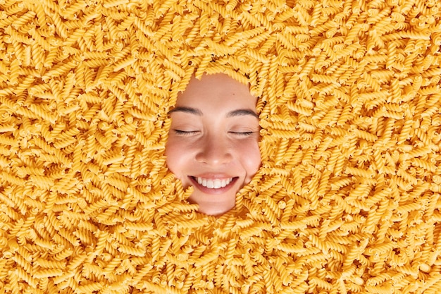 Free photo large pile of uncooked pasta around happy womans face. noodles made of durum wheat