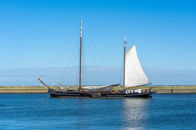 Large sailboat with white sails sailing on the water surface under a clear blue sky