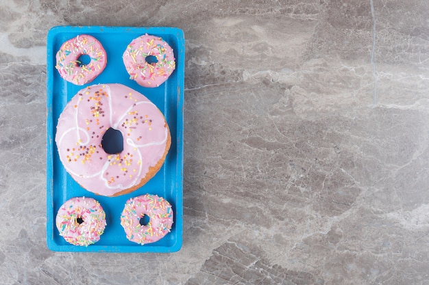 Large and small donuts arranged on a blue platter on marble surface