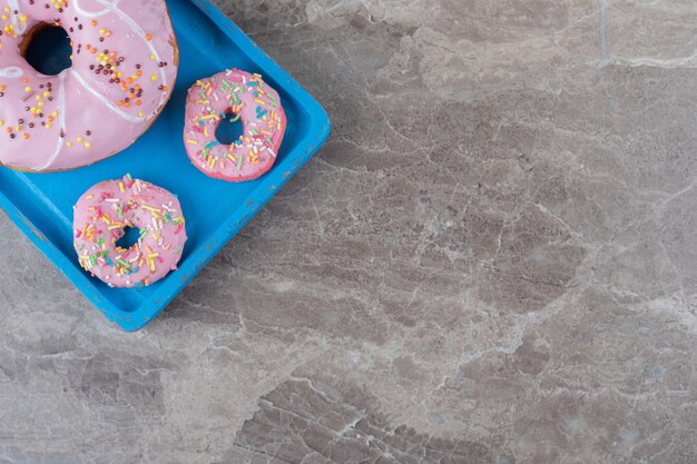 Large and small donuts arranged on a blue platter on marble surface