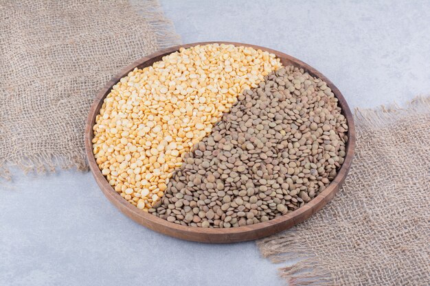 Large wooden tray filled with brown and red lentil on marble surface