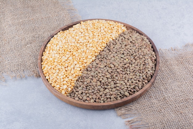 Large wooden tray filled with brown and red lentil on marble surface