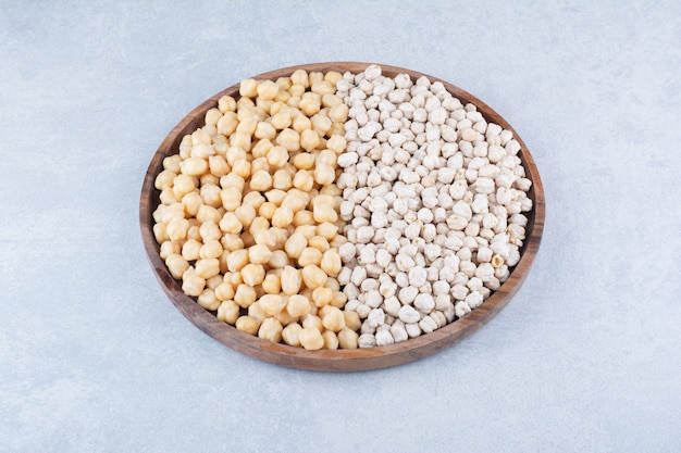 Large wooden tray stocked with piles of cooked and raw chickpeas on marble background.