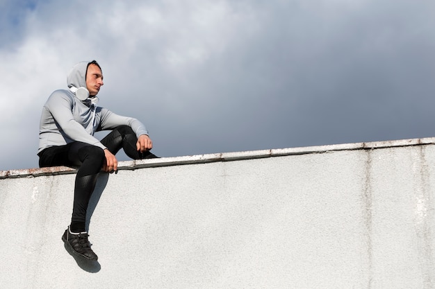 Lateral view man sitting on a wall and looking away