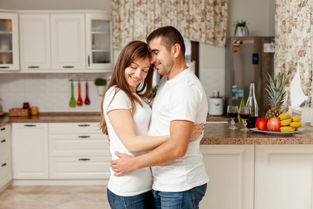 Lateral view smiling couple embracing in kitchen