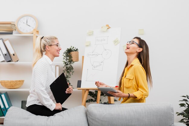 lateral view smiling women holding a tablet and a clipboard