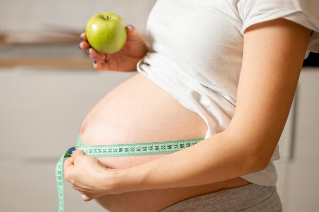 Lateral view woman hands holding an apple and measuring her belly