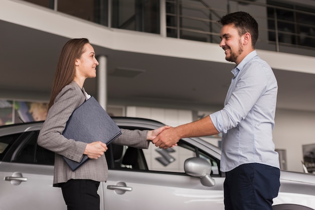 Lateral view young man shaking hands with car dealer