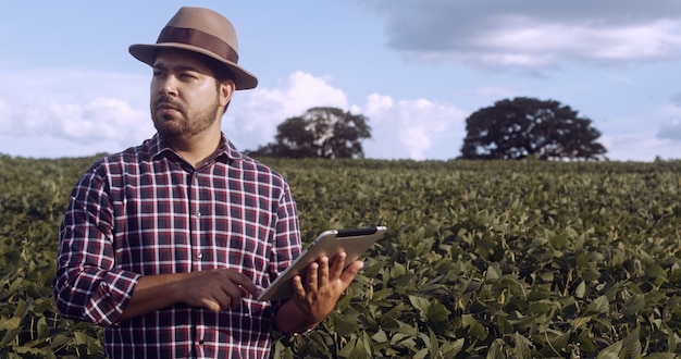Фермер из латинской америки, работающий на плантациях сои, изучает развитие урожая на планшете. Premium Фотографии