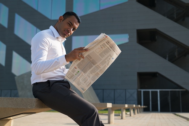 Latin Businessman Reading Newspaper Outside Office