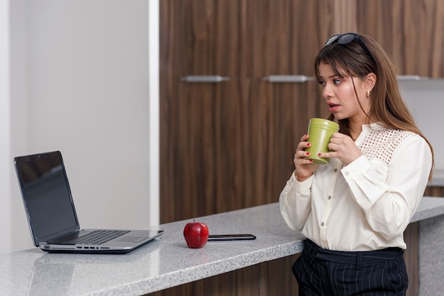 집에 있는 자신의 컴퓨터 개념을 작업하는 동안 커피를 마시는 라틴 여성