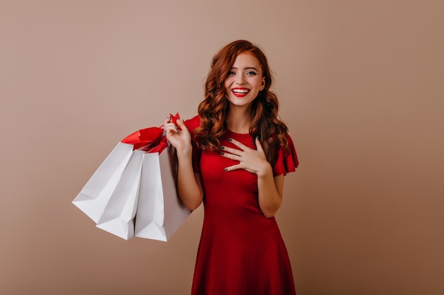 Laughing adorable girl holding paper bags from store. Magnificent caucasian lady posing  after shopping.
