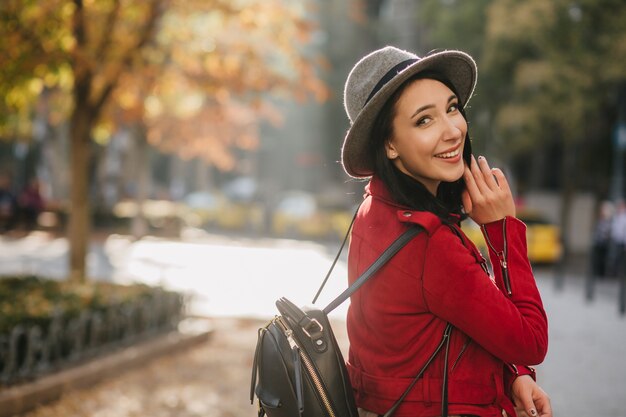 自然の壁に肩越しに見ているカジュアルな帽子で素晴らしい女性を笑う