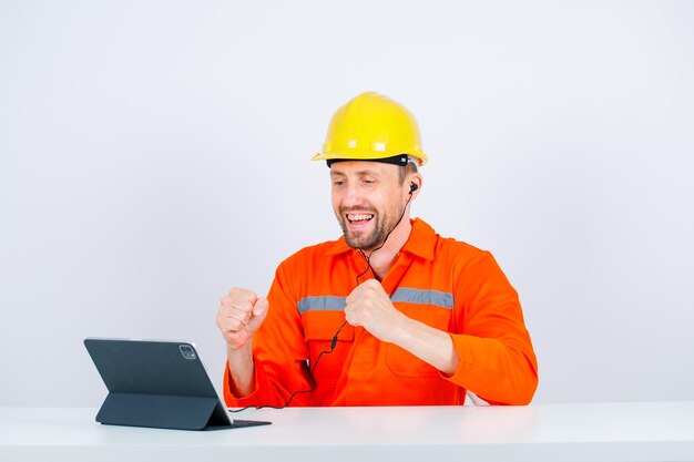 Laughing architect is raising up his fists by looking at tablet screen on white background