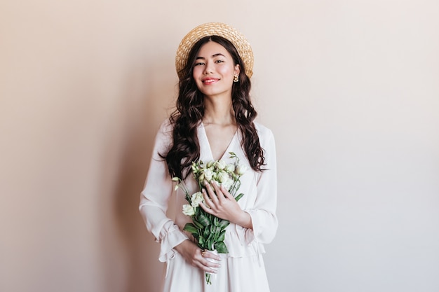 Laughing asian woman holding white flowers. Front view of japanese woman in straw hat posing with bouquet.
