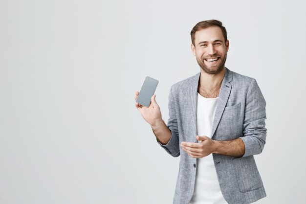 Смеющийся привлекательный мужчина, показывая экран смартфона