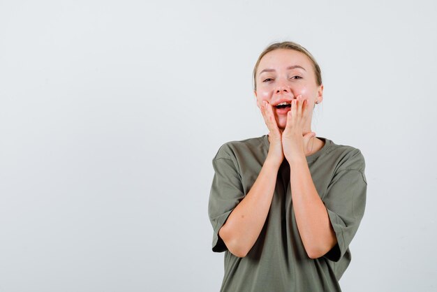 The laughing blonde woman is putting her hands on cheek on white background