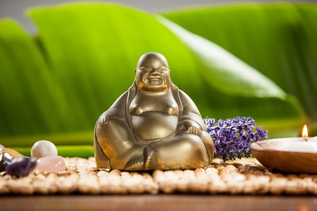 Laughing buddha figurine, lit candle and pebbles stone