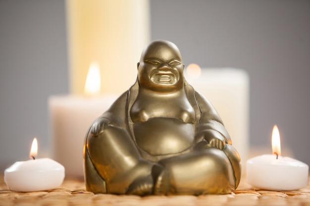 Laughing buddha figurine and lit candles on mat