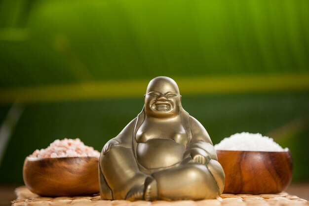 Laughing buddha figurine and sea salt in wooden bowl