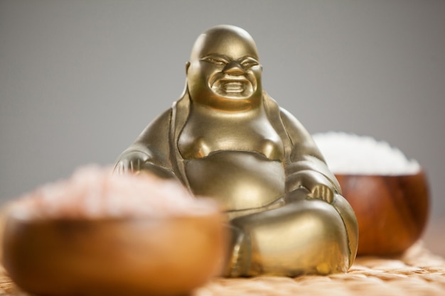 Free photo laughing buddha figurine and sea salt in wooden bowl