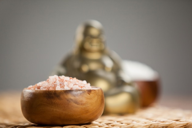 Laughing buddha figurine and sea salt in wooden bowl