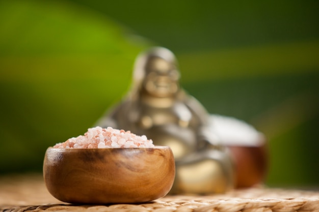 Laughing buddha figurine and sea salt in wooden bowl