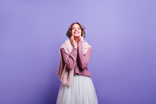 Laughing caucasian lady in winter accessories enjoying photoshoot. Magnificent white girl in lush vintage skirt posing in purple wall.