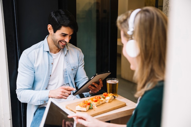 Laughing couple sitting with tablets in cafe