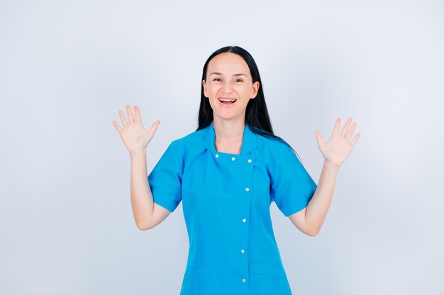 Laughing doctor is looking at camera by raising up her hands on white background