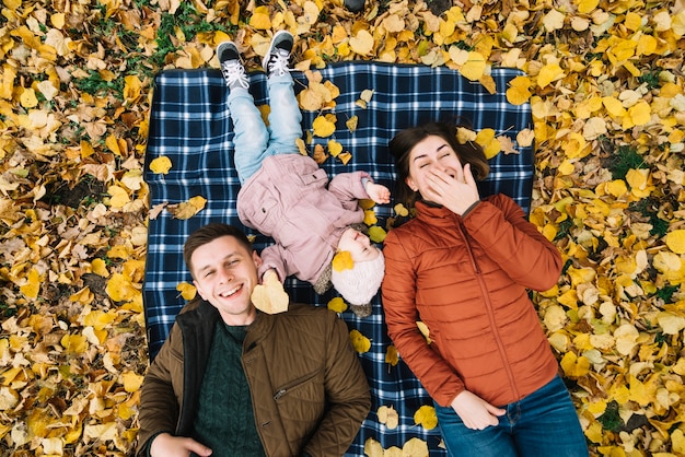 Laughing family lying on autumn ground with yellow leaves