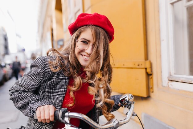 Смеющаяся женская модель со светло-каштановыми волосами веселится на велосипеде