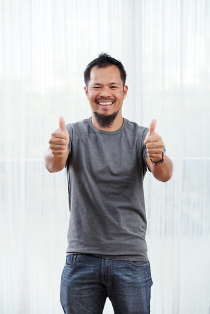 Laughing Filipino man standing in front of brightly lit window with his thumbs up